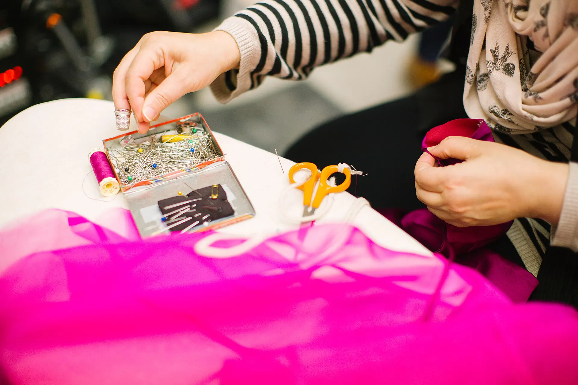 A seamstress pinning bright pink fabric at a worktable